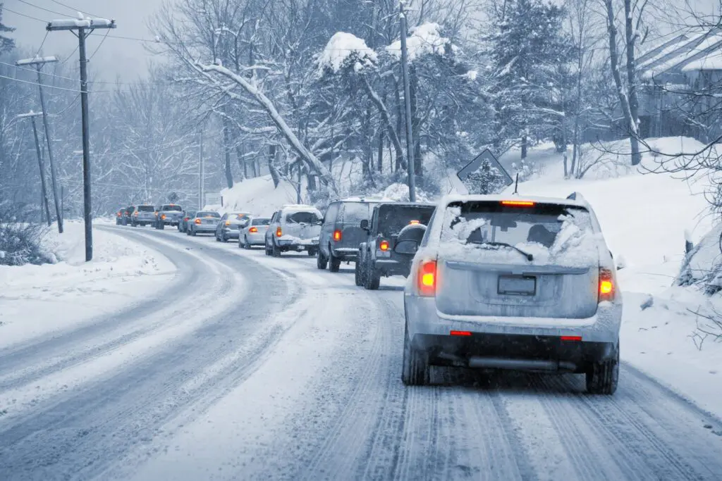 A line of cars driving cautiously down a snowy road