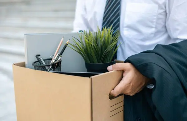 A businessman carrying a cardboard box filled with office supplies and a plant