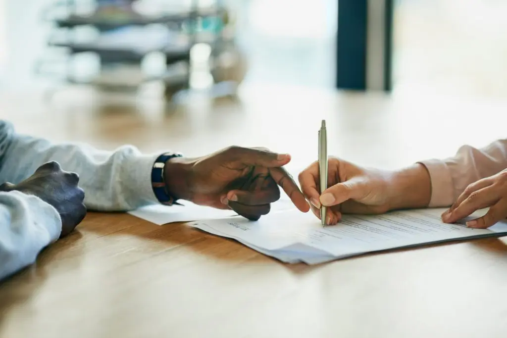 Two associates' hands pointing to and writing on a paper in an office