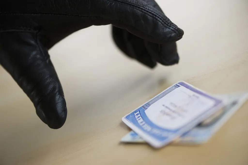 A gloved hand demonstrates identity theft by reaching for another person's Social Security card to steal it