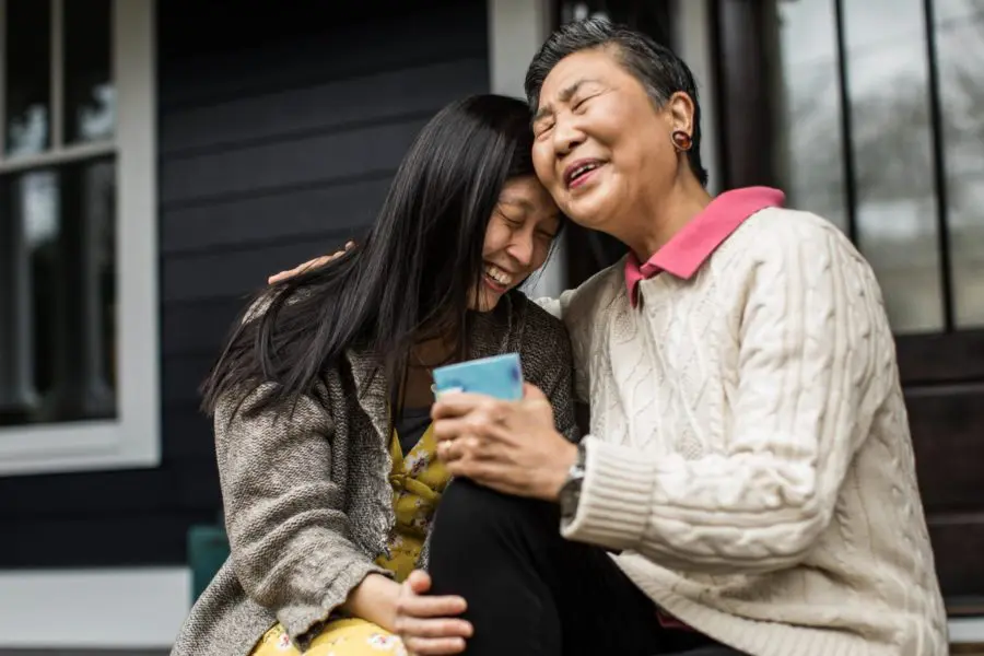 Grandmother and granddaughter laughing and sitting outside of house