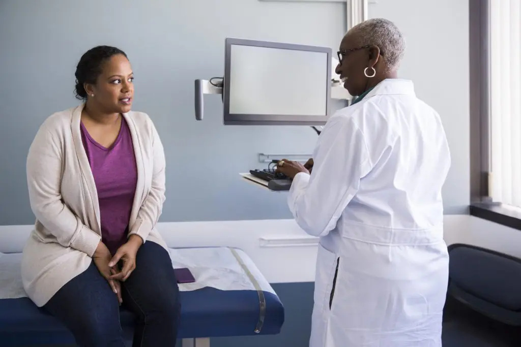 Concerned woman in medical office talking to a doctor smiling while typing on a computer