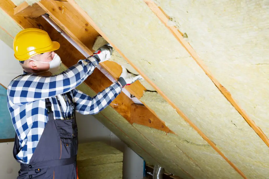 Handyman in protective gear installing insulation in a house attic