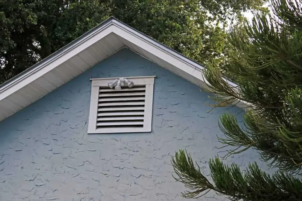 Top half of a house with shutters and a roof awning and floodlights surrounded by green trees