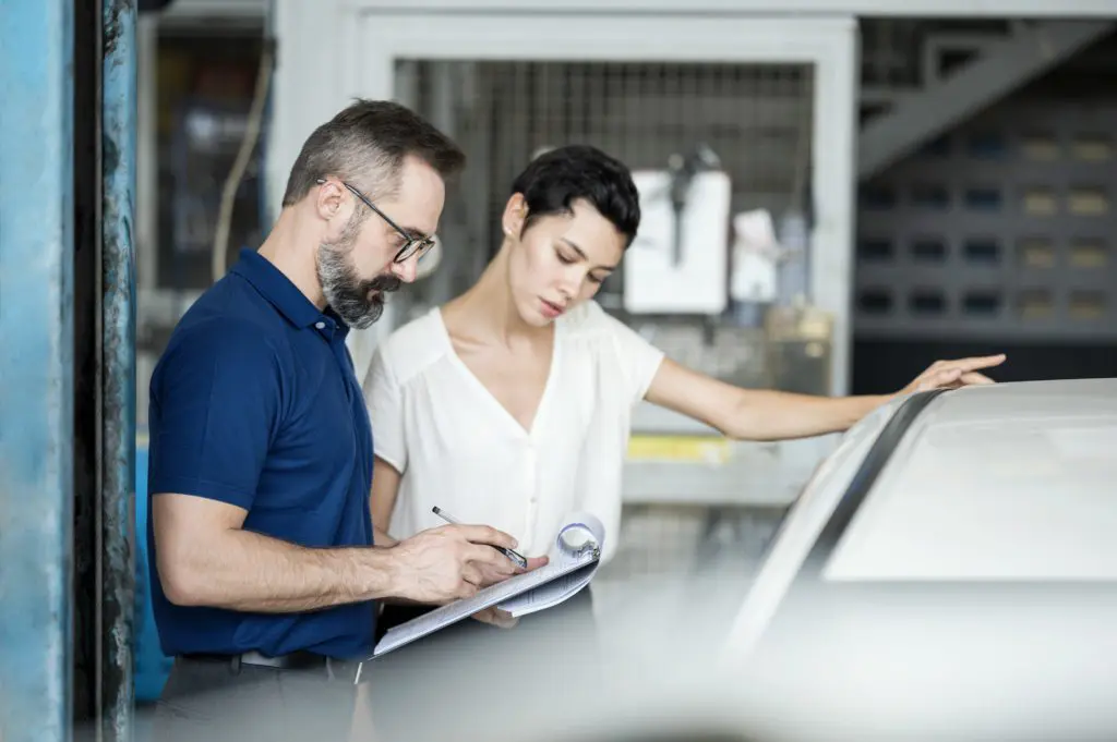 Mechanic and woman in auto repair shop looking at a clipboard next to a car
