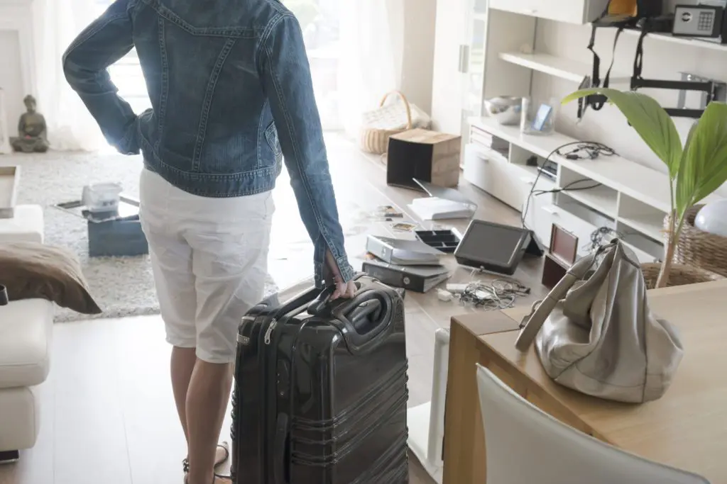 Woman walking into apartment with suitcase to see belongings scattered and ransacked