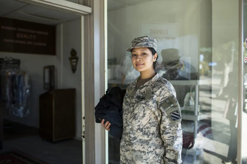 Woman in military uniform standing outside dry cleaning business with laundry bag