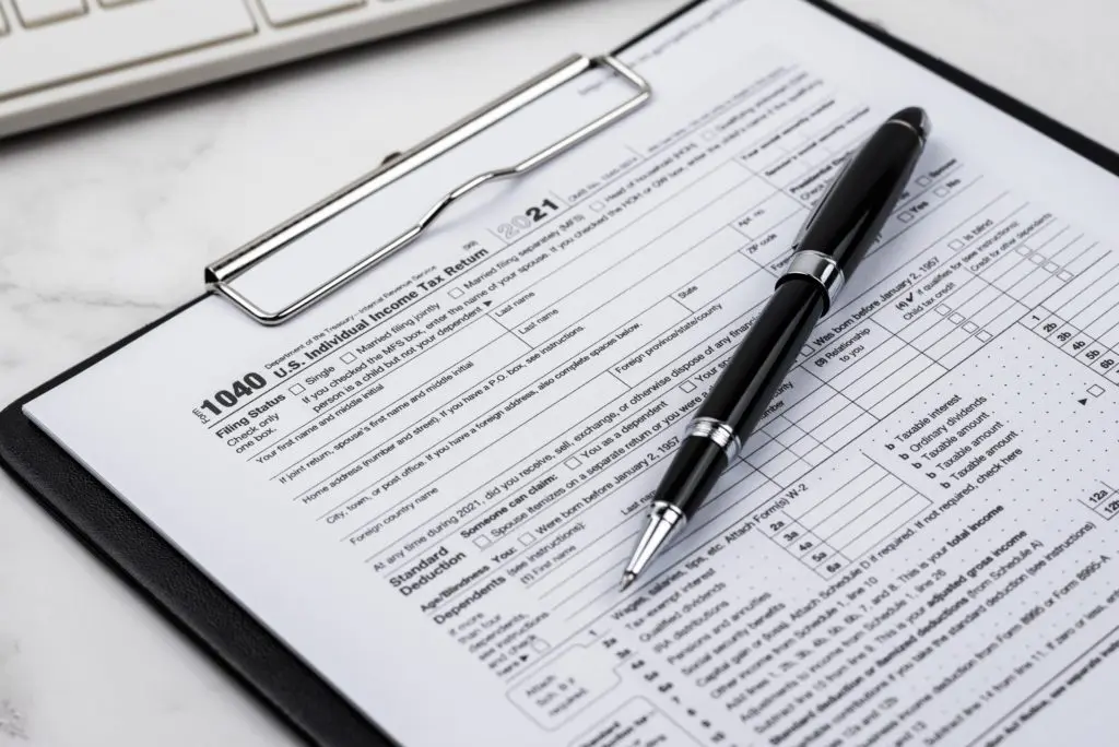 Clipboard holding 1040 tax paperwork on desk with a pen