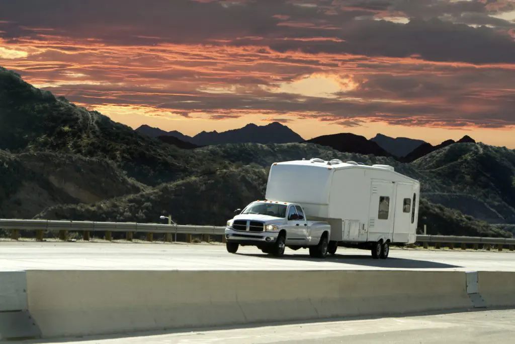 Truck pulling an RV driving down an open road surrounded by mountains