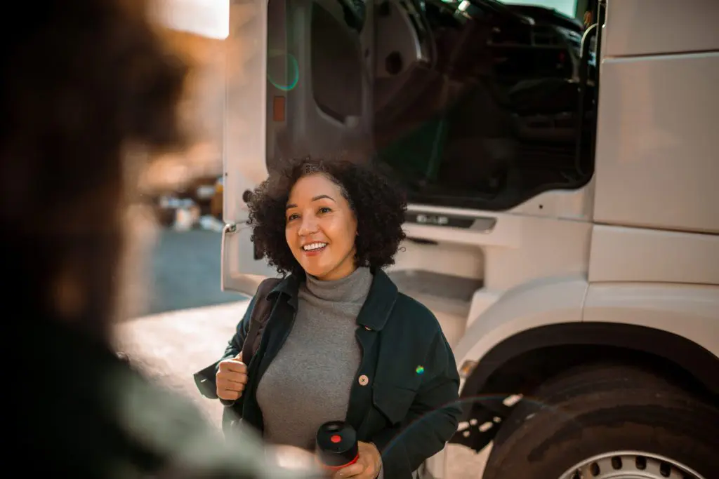 Woman smiling standing outside truck cab talking to an associate