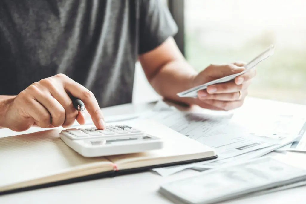 Person holding receipts with scattered bills and paperwork doing math on a calculator