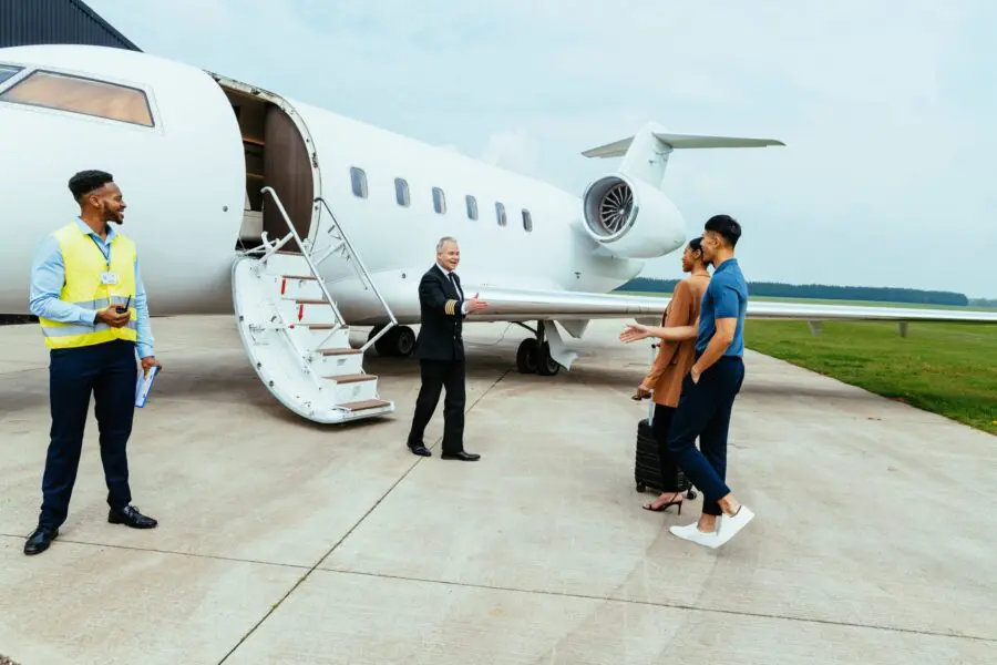 Passengers arriving in private luxury jet near hangar, pilot welcomes the young successful passengers