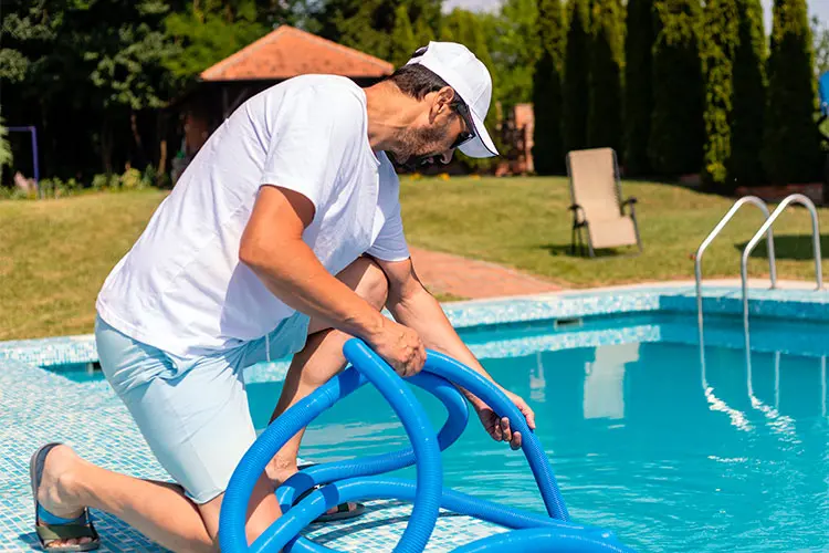 Man kneeling over home pool using equipment to clean and maintain pool