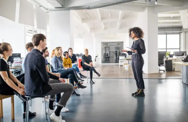 Young businesswoman addressing colleagues in meeting in large office