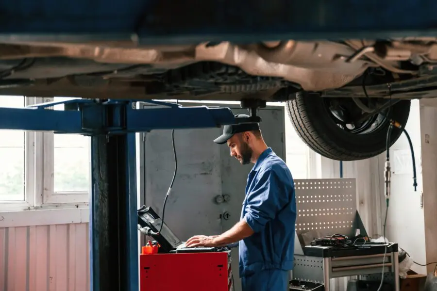 Using laptop and testing device. Auto mechanic working in garage. Repair service.