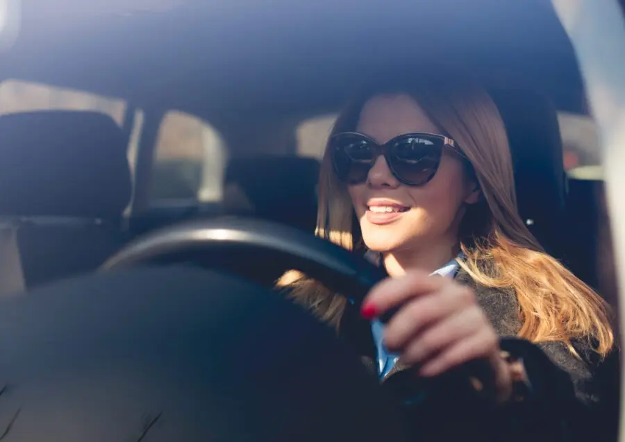 Smiled woman driving car through city.
