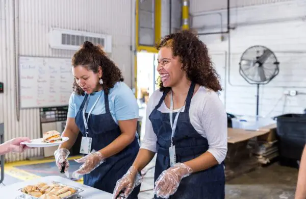 The female volunteers serve sandwiches to the homeless at the shelter.
