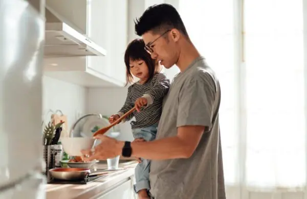 Asian stay-at-home dad teaching his little daughter cooking in kitchen at home. Modern manhood and fatherhood. Healthy family lifestyle.