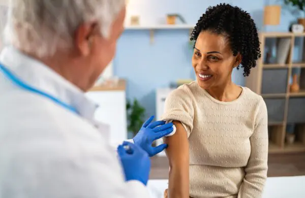 Senior Caucasian male doctor, giving a flu vaccine to a female patient African-American ethnicity, during an annual medical check-up