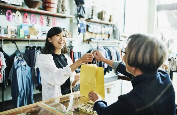 Shop owner handing bag to client after shopping in clothing boutique