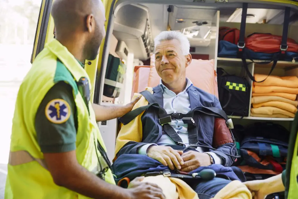 Elderly man smiling on a stretcher being comforted by paramedic while loading into ambulance