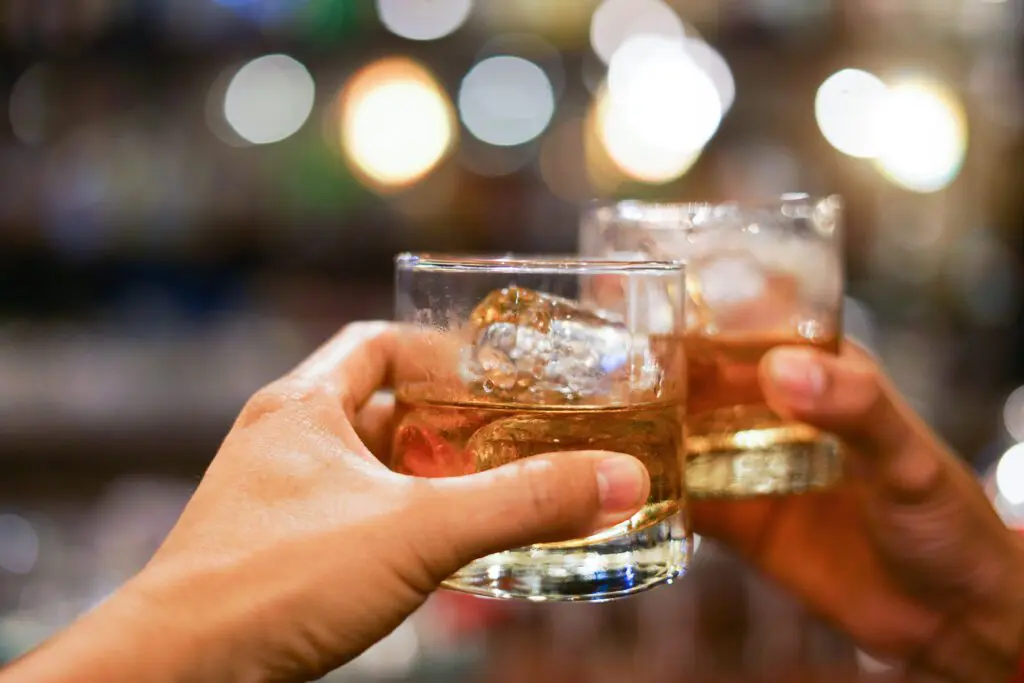 Two men clinking glasses of whiskey or similar liquor together at a counter in the pub