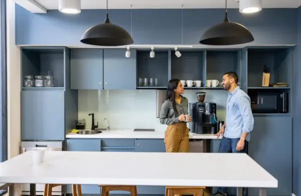 Happy coworkers talking in the breakroom area near a coffee pot while taking a break at the office