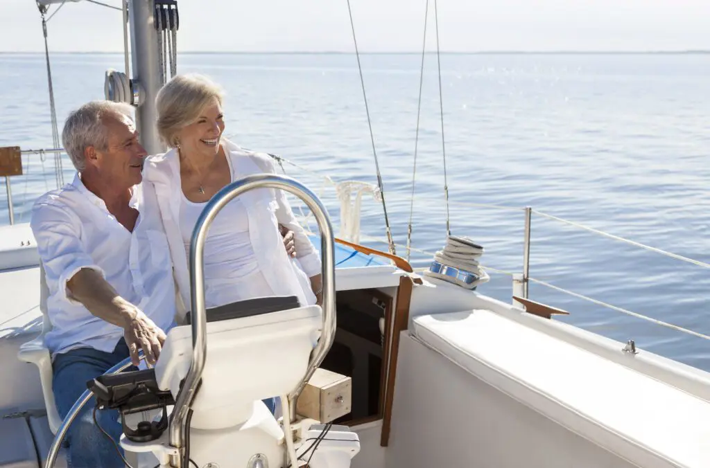 A happy senior couple sailing and sitting at the wheel of a yacht on a calm blue sea