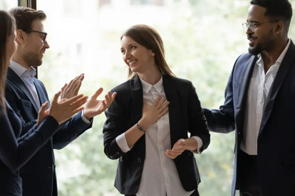 Diverse multiethnic businesspeople applaud greeting with promotion young female colleague at meeting, multiracial coworkers clap hands thanking for presentation or business success to woman employee