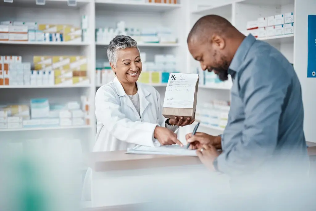 Pharmacist assisting male customer while shopping for medicine in pharmacy and writing medical information for prescription