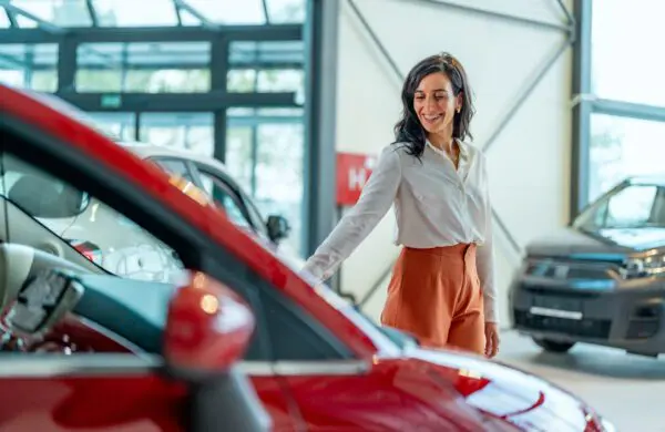 Businesswoman looking for a new car, standing next to a new SUV indoors at a car dealer