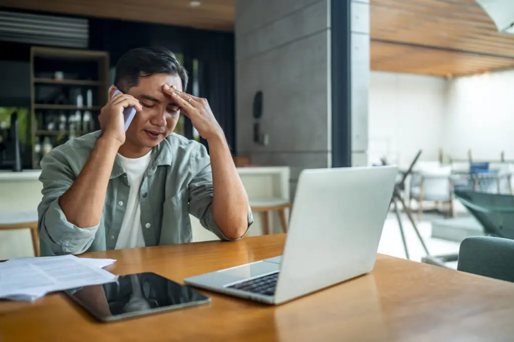 Businessman on a phone call at home rubbing his forehead in frustration