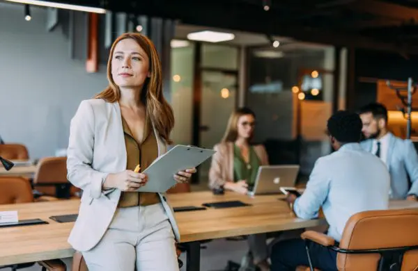 Business woman holding a clipboard with her colleagues in the background during a meeting in board room