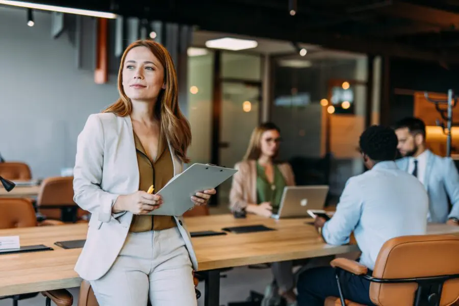 Business woman holding a clipboard with her colleagues in the background during a meeting in board room