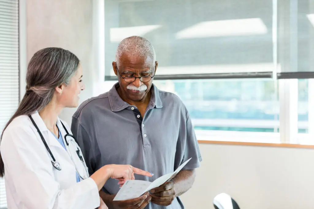 A doctor discusses Medicare health insurance paperwork with an older man in a medical office setting