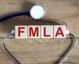 Wooden blocks spelling "FMLA" with a stethoscope on a wooden surface, highlighting the Family and Medical Leave Act in healthcare—relevant for the April 2025 HR Update.
