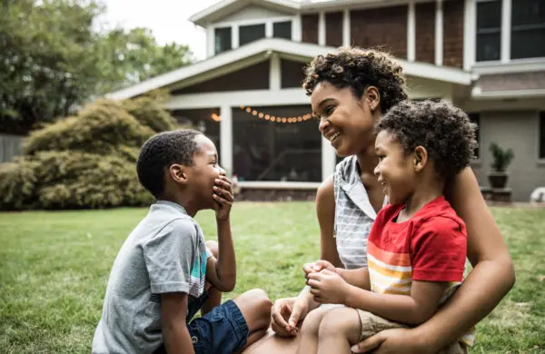 Single mother playing with young sons in front of house