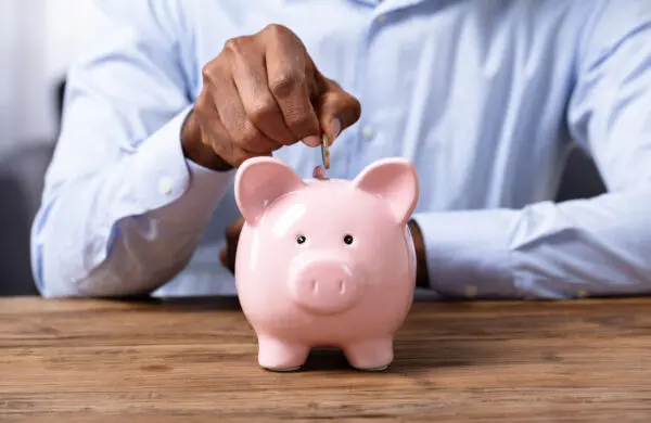 African American man's hands saving money by placing currency into a pink piggy bank