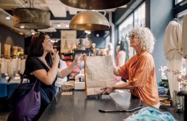 Senior female small business owner giving a bag to customer at checkout in retail store