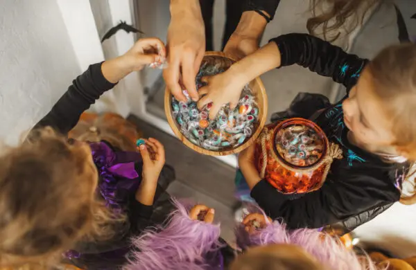 Children in costumes trick-or-treating and receiving candy on Halloween