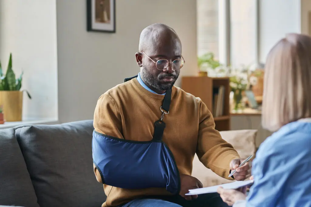 African American man with broken arm signing contract for at home medical services on clipboard