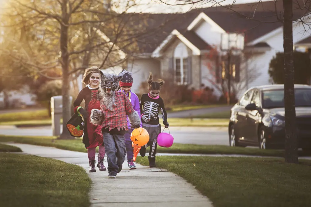 Group of children wearing Halloween costumes walking on a neighborhood sidewalk while trick-or-treating
