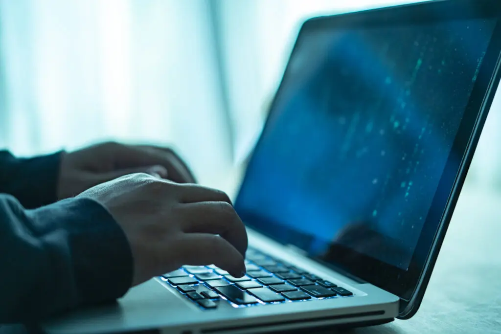 Hacker's hands typing on laptop computer while committing cyber fraud
