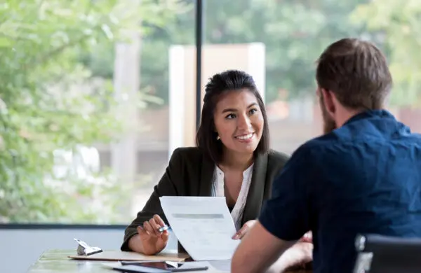 Hispanic businesswoman smiles while showing a document to a male associate