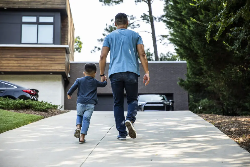 Father walking up the driveway of a modern home with his son