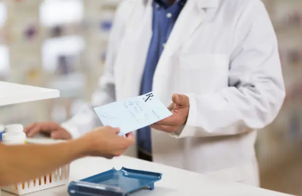 A man handing a handwritten prescription to a pharmacist