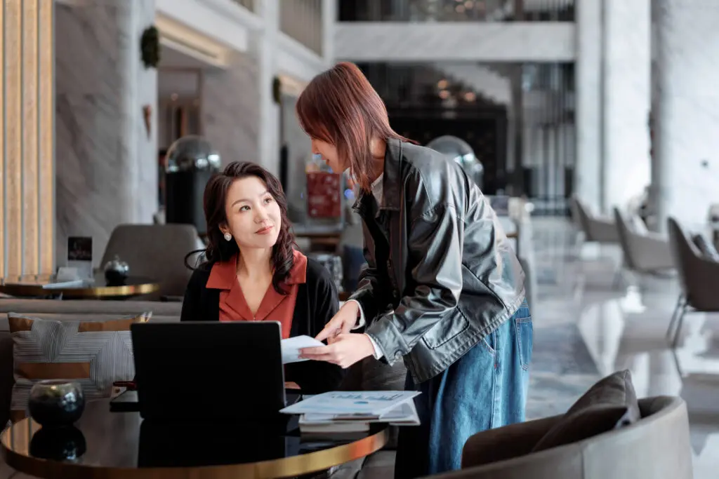A young intern leans forward while presenting ideas to her supervisor, who listens attentively in a business lounge