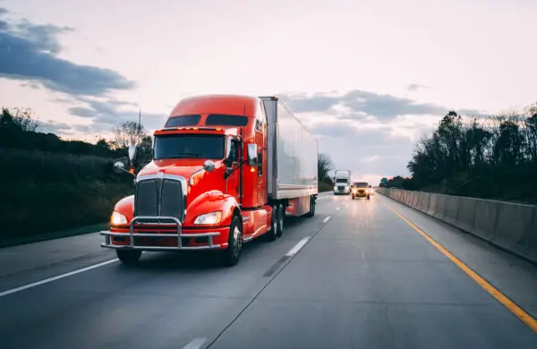 Orange 18 wheeler semi truck delivering goods on the road at night with headlights