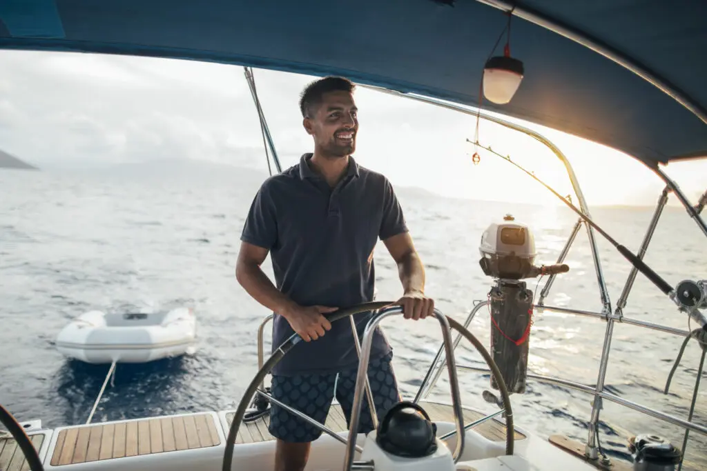 Smiling young helmsman steering a sailboat on a body of water