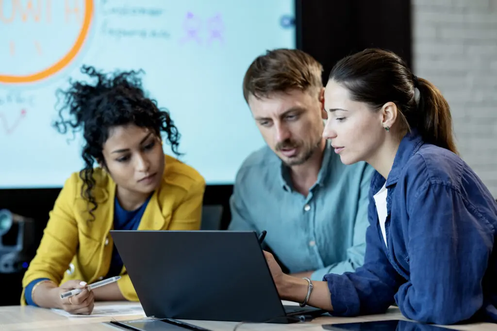 Team of business leaders discuss over a laptop computer in a strategy meeting